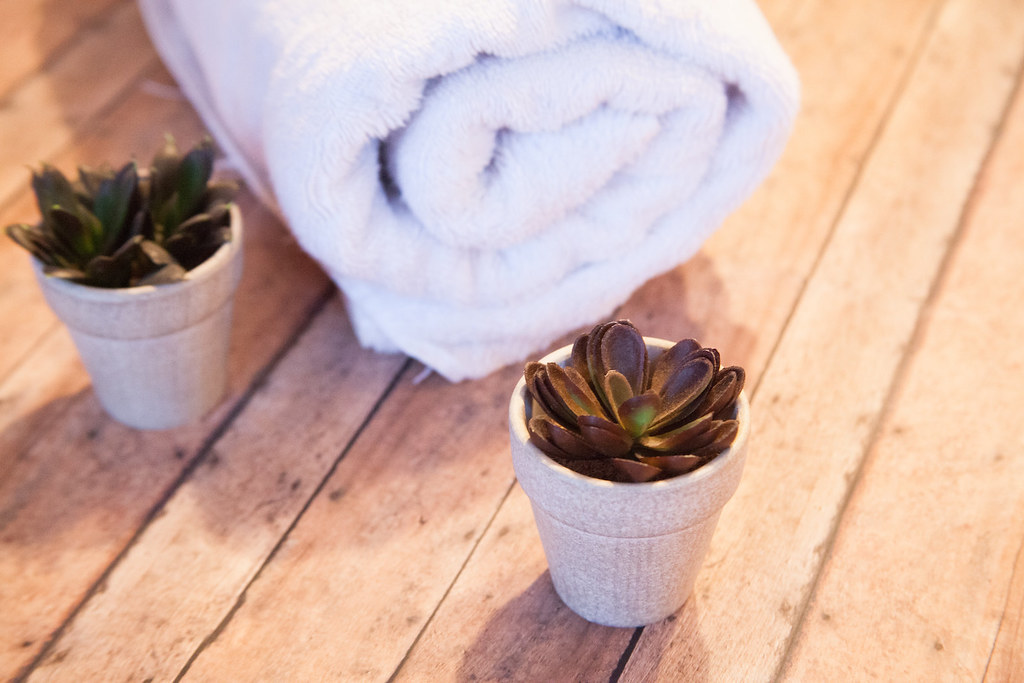 Rolled white spa towel with small potted botanicals on a warm wooden surface