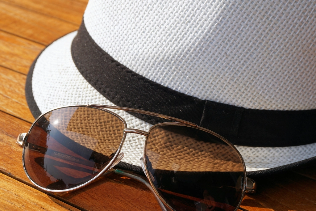 Sun hat and sunglasses on a wooden surface for simple summer pool bag essentials