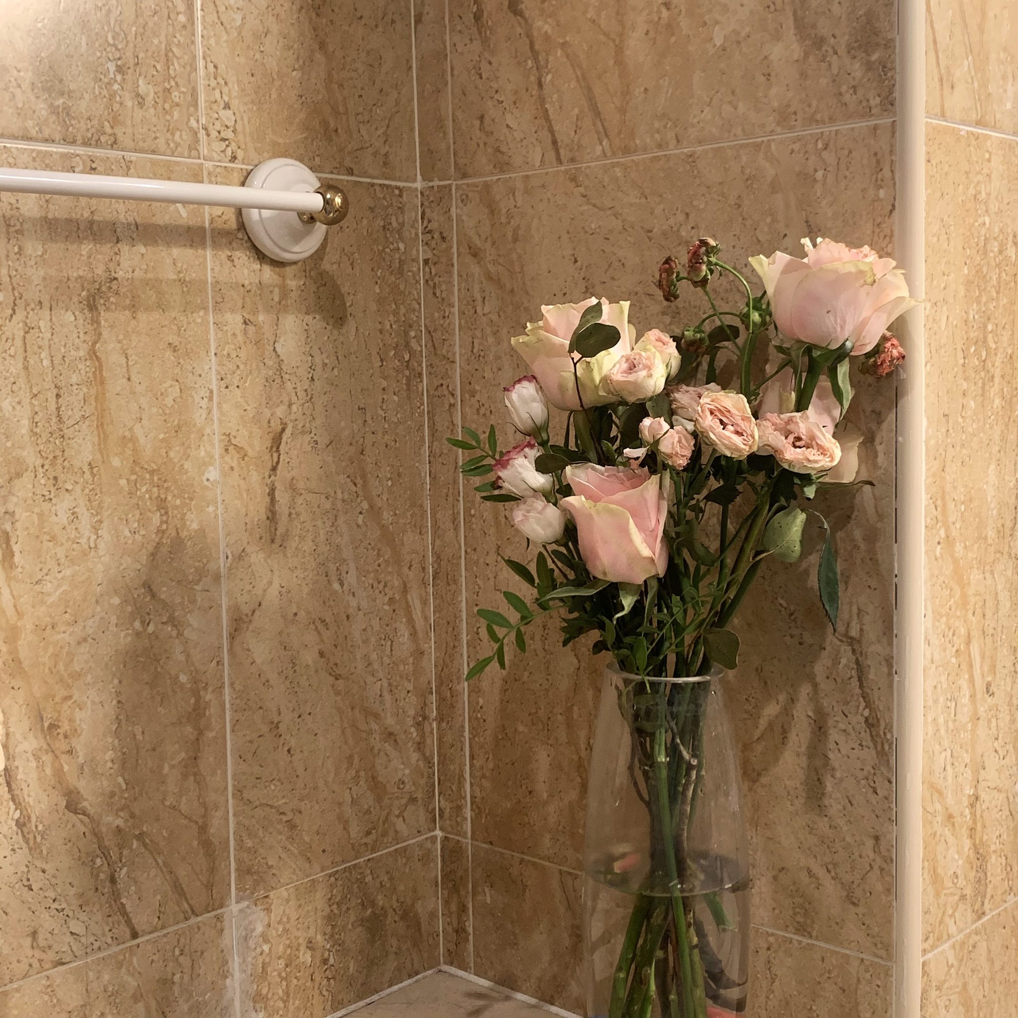Pink roses beside an empty towel rail in a warm tiled bathroom