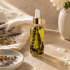 Pale golden botanical oil in a clear glass dropper bottle with dark flower stems