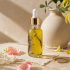 Golden botanical face and body oil in a clear glass dropper bottle with decorative metallic accents