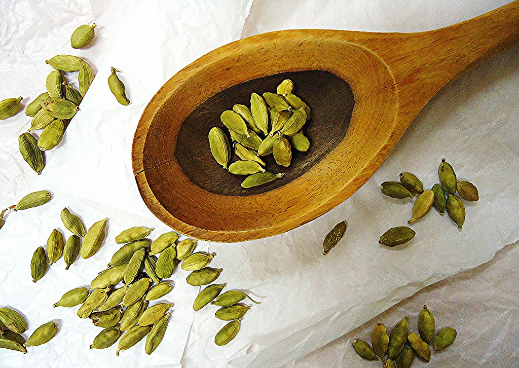 Green cardamom pods scattered around a wooden spoon on a pale background