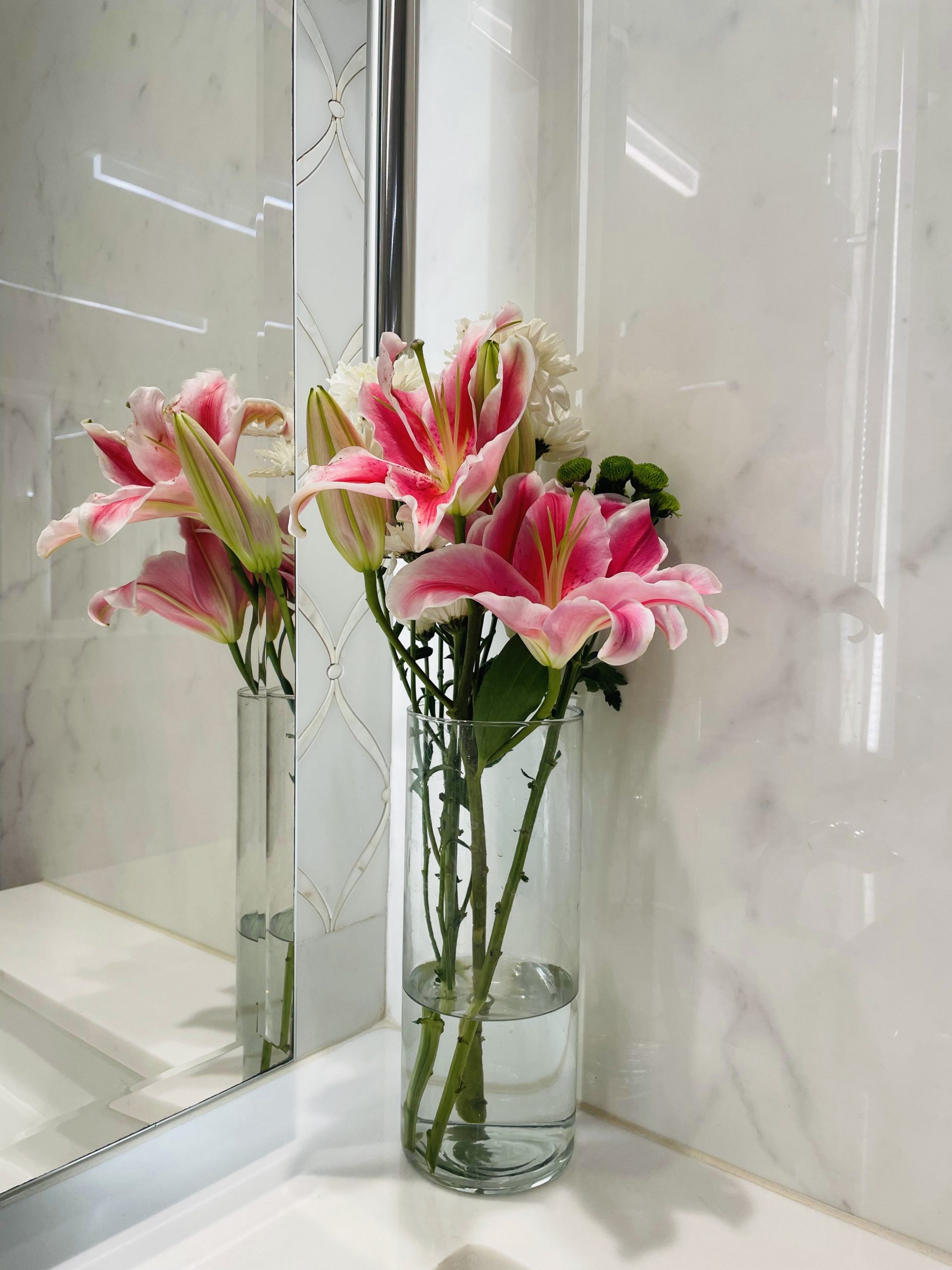 Pink lilies in a clear glass vase on a bathroom counter beside a mirror